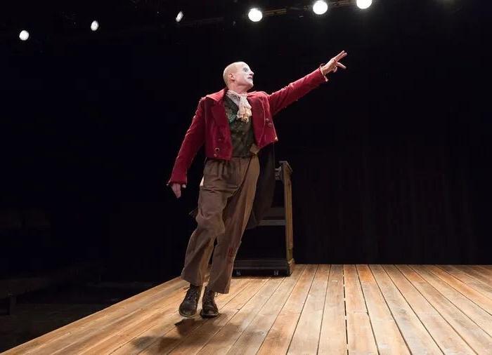 A single actor on a stage in a red jacket